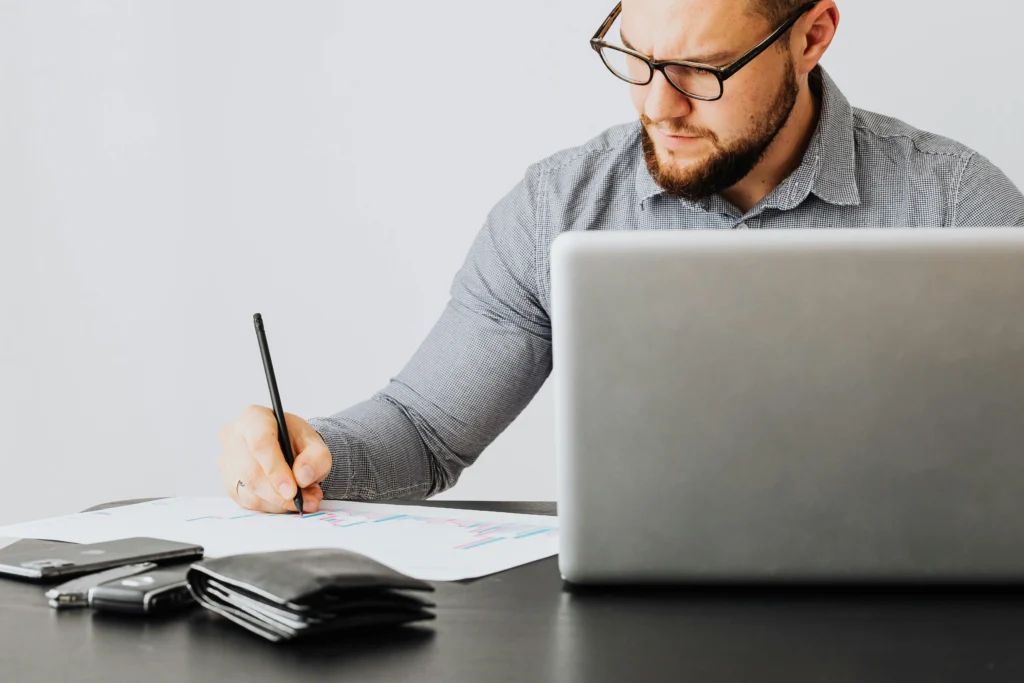 Profesional con anteojos revisando gráficos junto a su laptop, representando orden y toma de decisiones